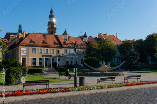 Old Town Square (Rynek or Market Square) early in the morning, ray of sunshine. Tower Of Church of the Assumption of St. Mary in background. Town in Silesia Province. Wodzislaw Slaski, Poland.