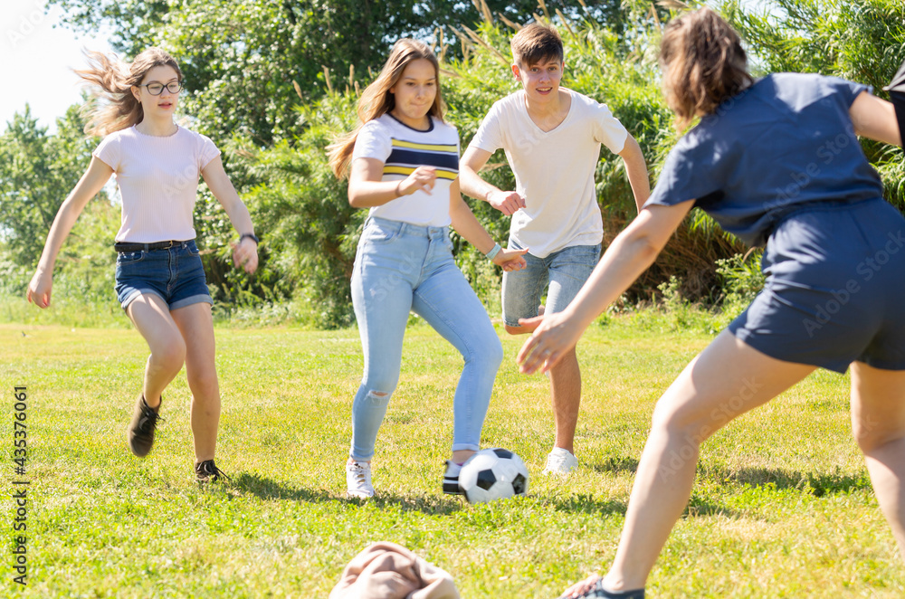 Obraz premium Company of glad teenagers playing football in park