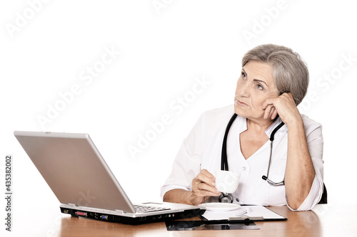 Serious elderly woman doctor sitting at table with computer