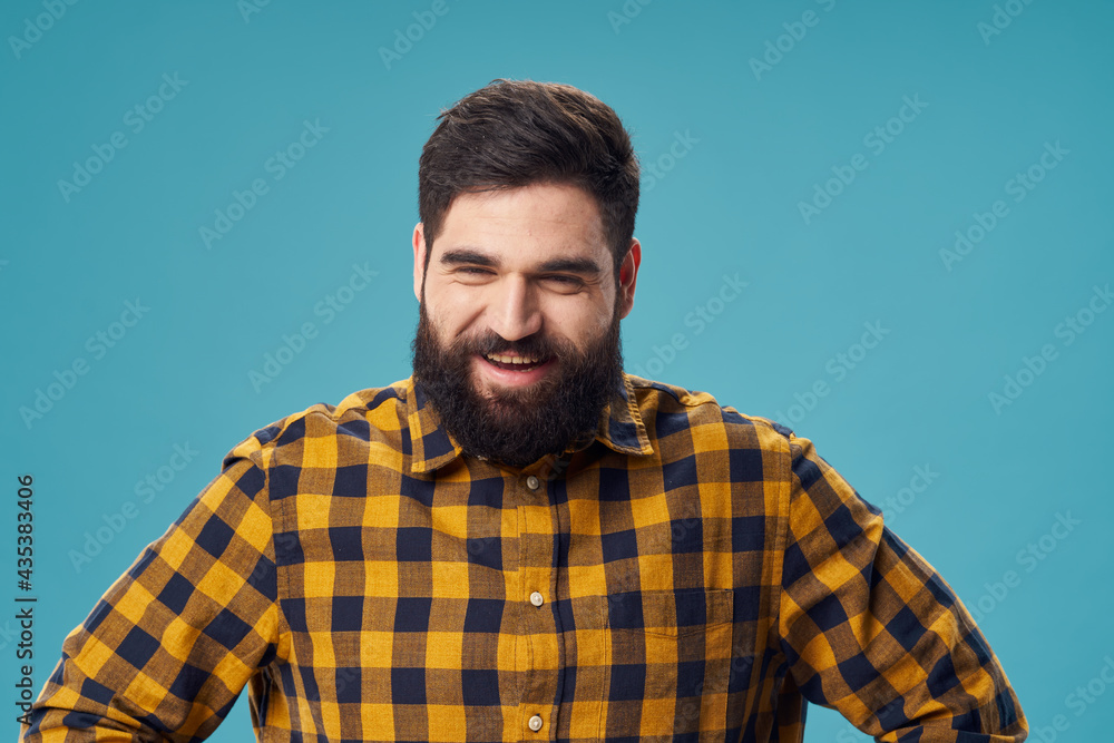 a man with a beard and a plaid shirt holds his hands on his belt on a blue background