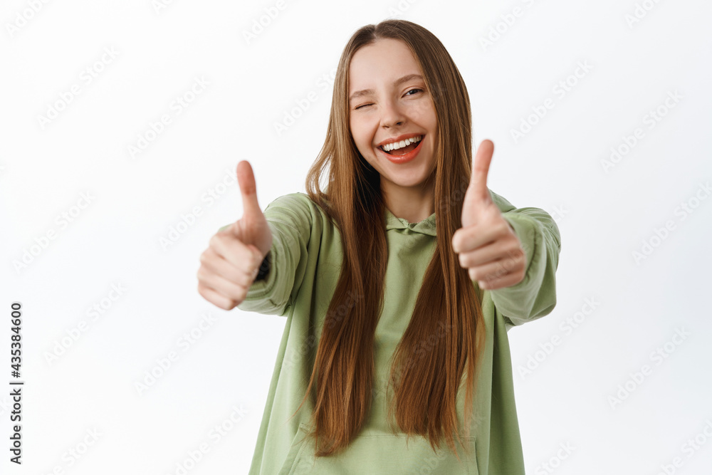 Carefree young woman stretch thumbs up and wink at you, praise good work, excellent job, recommend something cool, like and say yes, standing over white background Carefree young woman stretch thumbs up and wink at you, praise good work, excellent job, recommend something cool, like and say yes, standing over white background