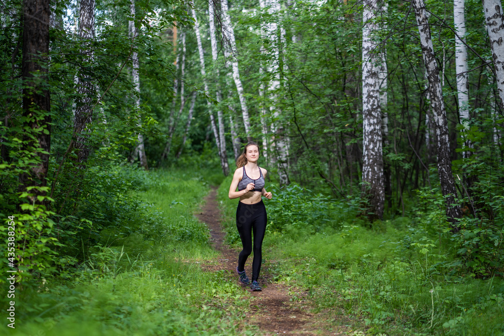 Sporty young brunette woman jogging in the woods. The sportswoman goes in for sports in the fresh air.