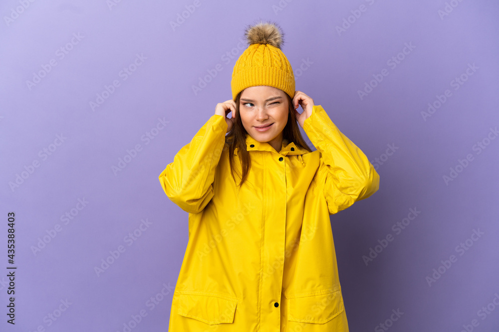 Teenager girl wearing a rainproof coat over isolated purple background frustrated and covering ears Teenager girl wearing a rainproof coat over isolated purple background frustrated and covering ears