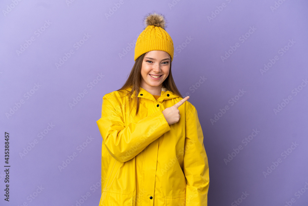 Teenager girl wearing a rainproof coat over isolated purple background pointing to the side to present a product Teenager girl wearing a rainproof coat over isolated purple background pointing to the side to present a product