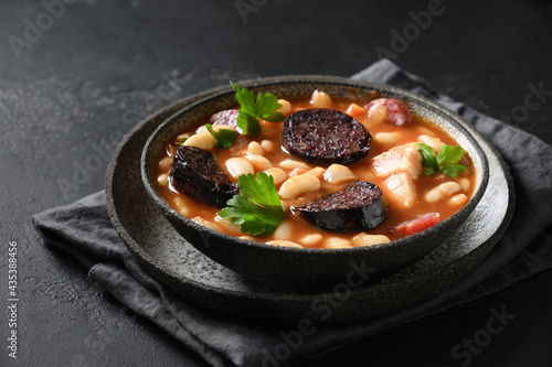 Spanish fabada with chorizo, morcilla, sausage, haricot served fresh toast on black background with copy space. Close up. Tasty traditional warming dinner.
