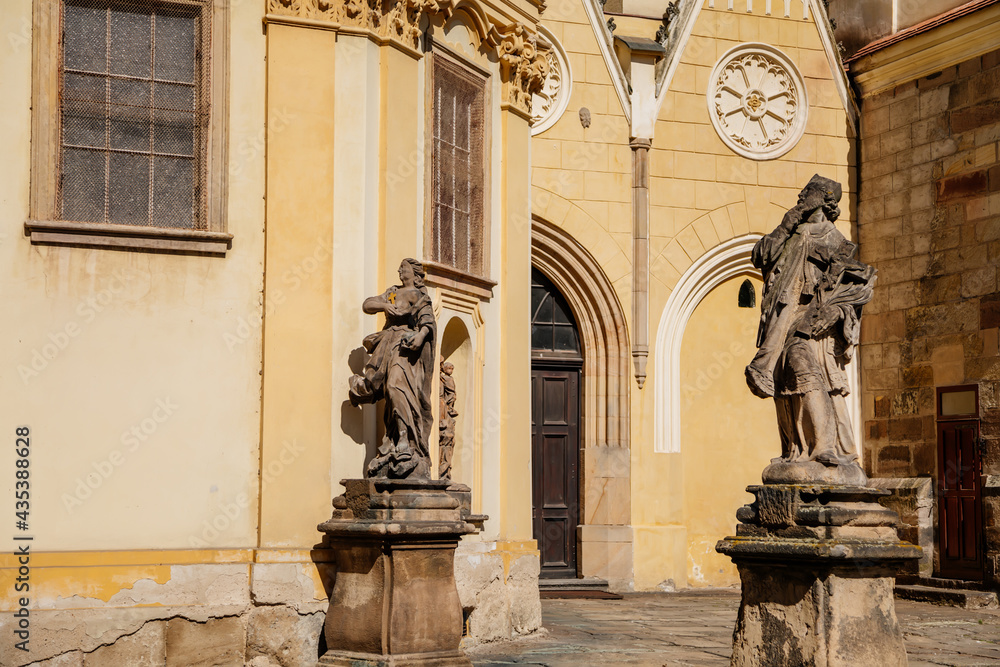 Church of Assumption of Blessed Virgin Mary, baroque sculptural group at Hostalkovo namesti, Medieval street, gothic portal, stone carving, sunny day, Zatec, Bohemia, Czech Republic