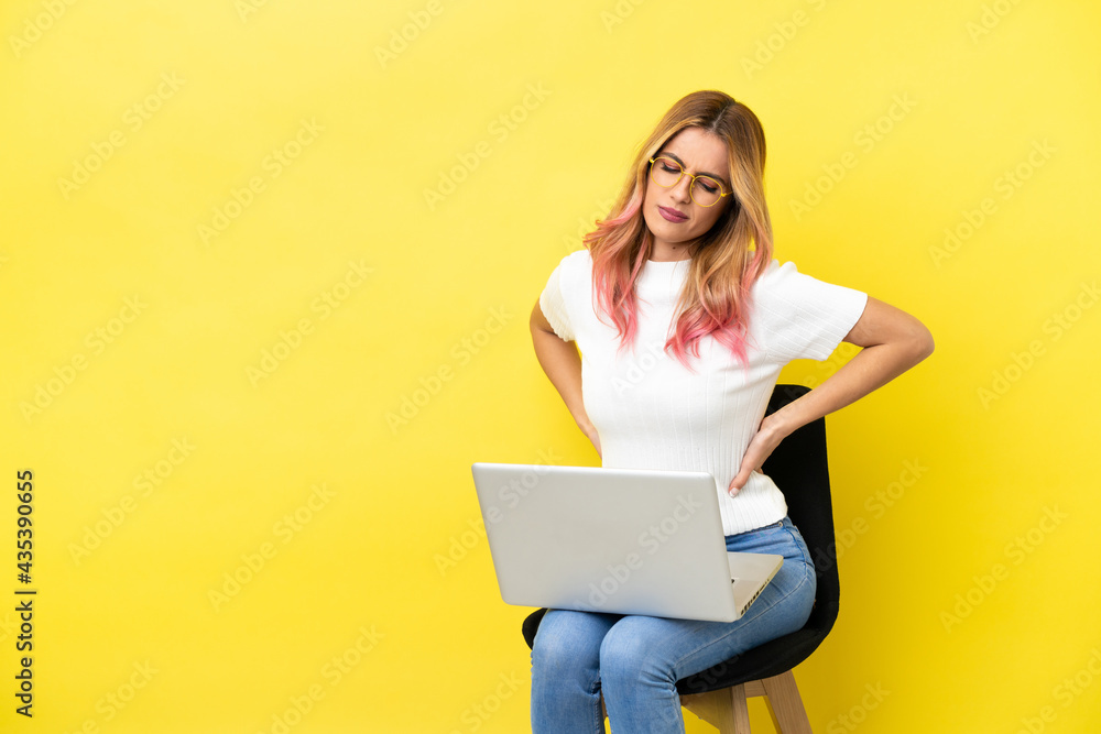 Naklejka premium Young woman sitting on a chair with laptop over isolated yellow background suffering from backache for having made an effort
