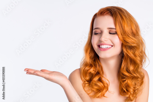 Photo portrait of pretty girl with curly red hair smiling looking keeping blank space on hand isolated on white color background