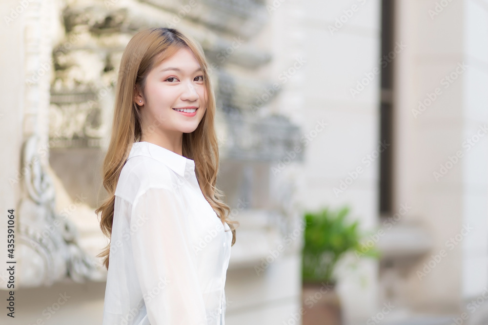 Portrait Asian beautiful woman with long bronze hair in white long sleeve shirt stand smile in an urban outdoor park. Portrait Asian beautiful woman with long bronze hair in white long sleeve shirt stand smile in an urban outdoor park.