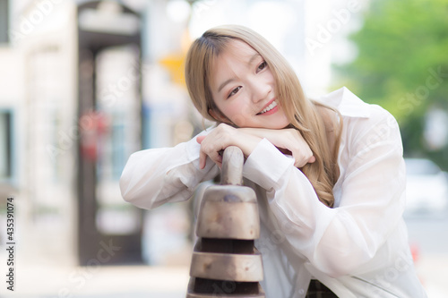 Asian beautiful woman with bronze hair in white shirt while sits happy smilie on the edge of a city street.