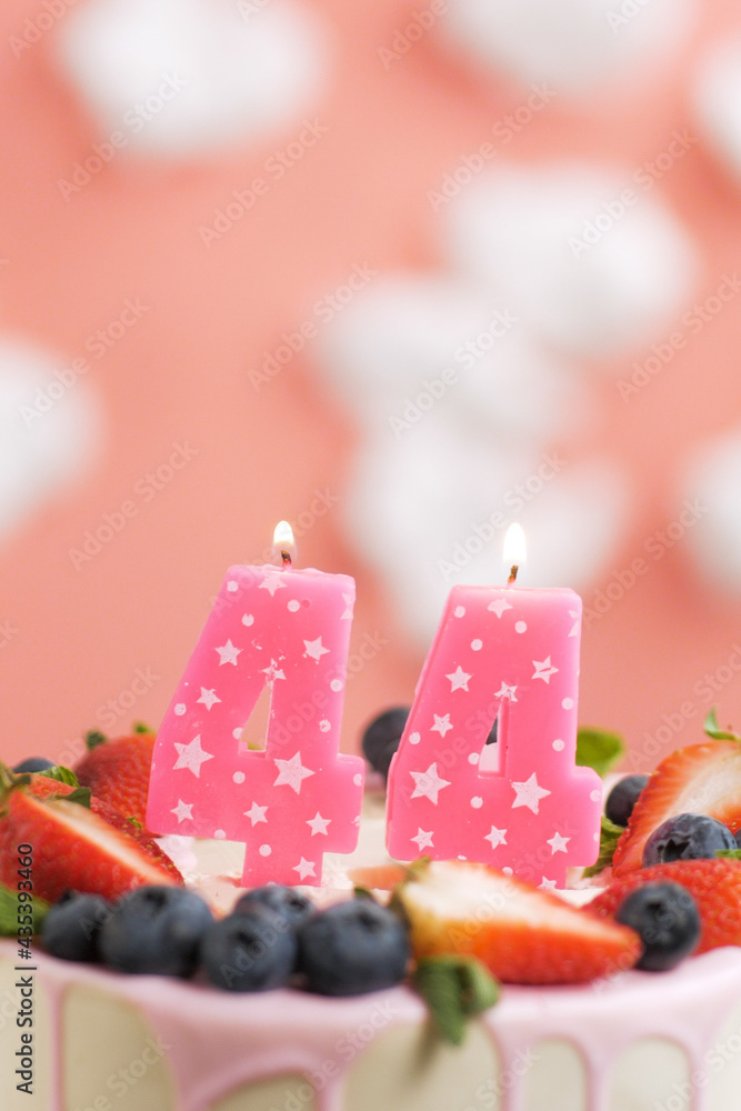 Birthday cake number 44. Beautiful pink candle in cake on pink background with white clouds. Close-up and vertical view