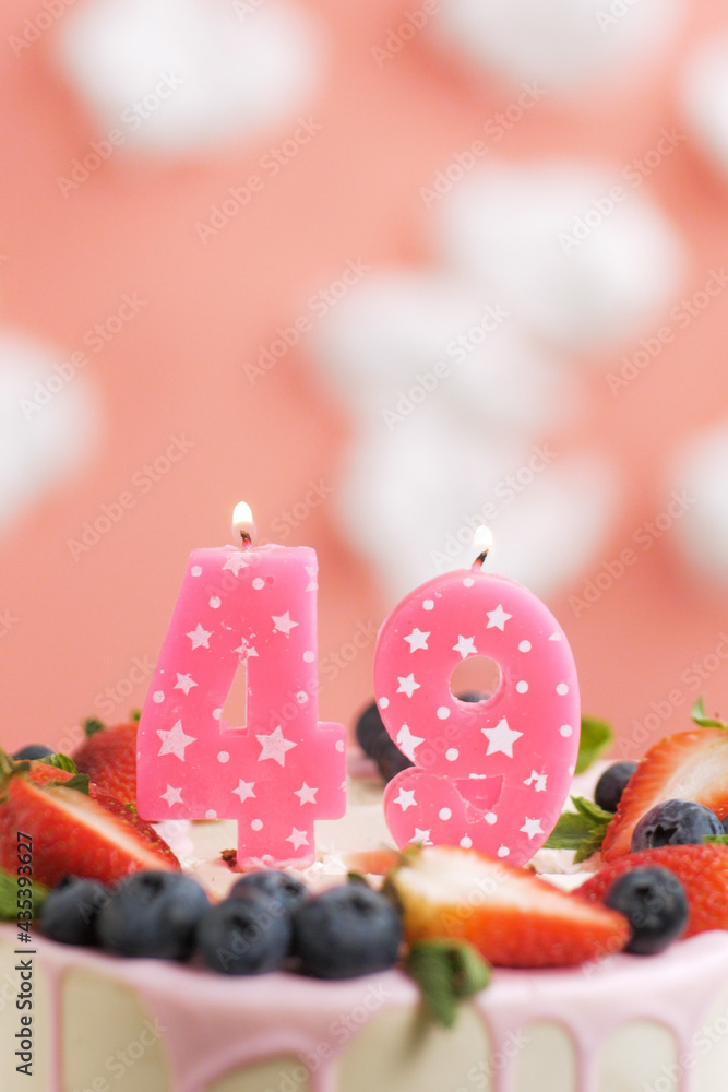Birthday cake number 49. Beautiful pink candle in cake on pink background with white clouds. Close-up and vertical view