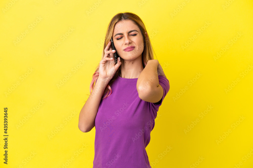 Young woman using mobile phone over isolated yellow background suffering from pain in shoulder for having made an effort Young woman using mobile phone over isolated yellow background suffering from pain in shoulder for having made an effort