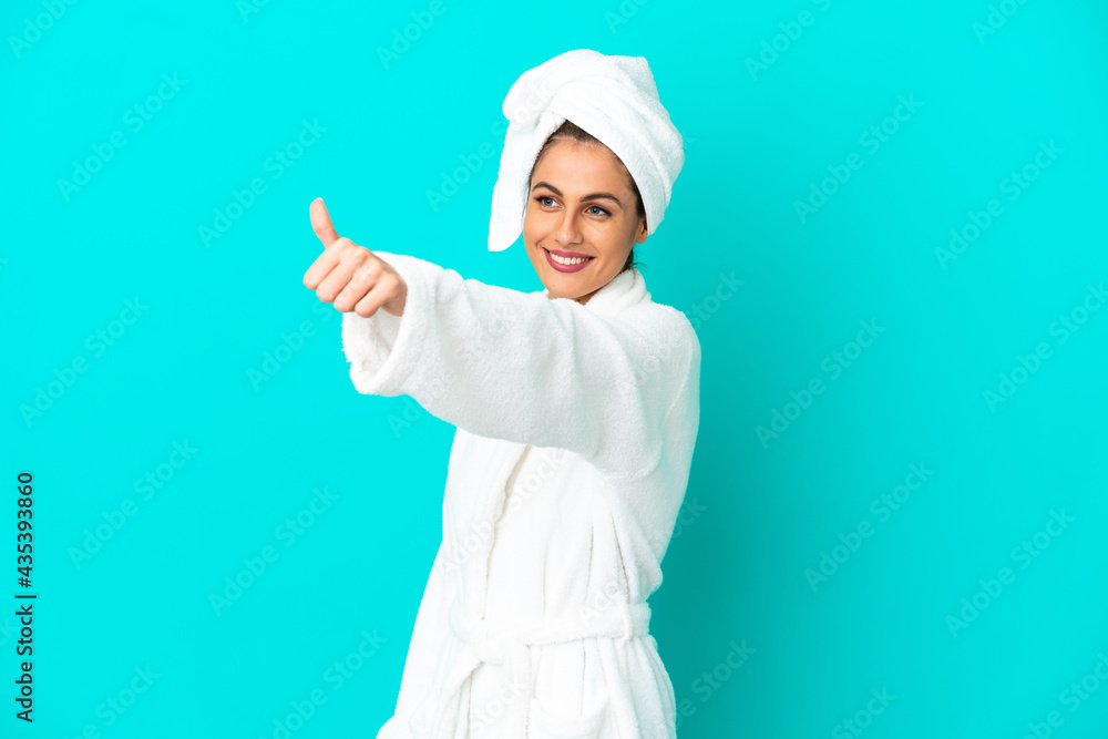 Young woman in a bathrobe over isolated blue background giving a thumbs up gesture Young woman in a bathrobe over isolated blue background giving a thumbs up gesture
