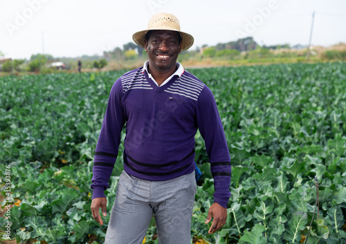 Portrait of smiling afro american man farmer in straw hat standing in farm field on sunny spring day