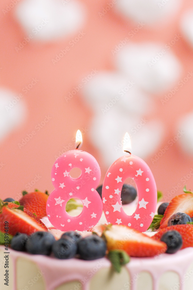 Birthday cake number 80. Beautiful pink candle in cake on pink background with white clouds. Close-up and vertical view