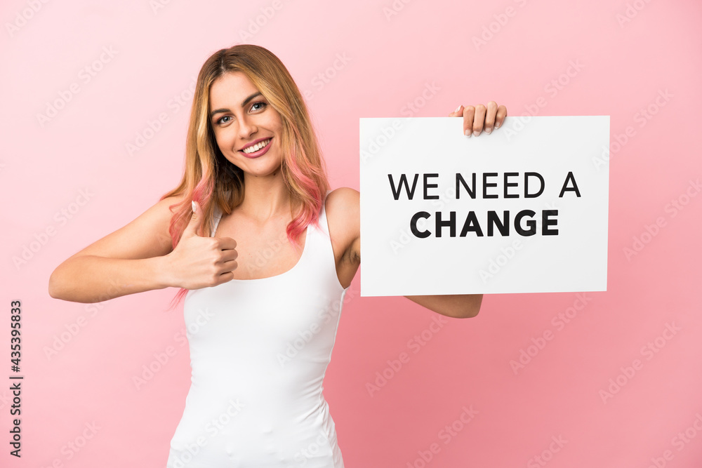 Young woman over isolated pink background holding a placard with text We Need a Change with thumb up Young woman over isolated pink background holding a placard with text We Need a Change with thumb up