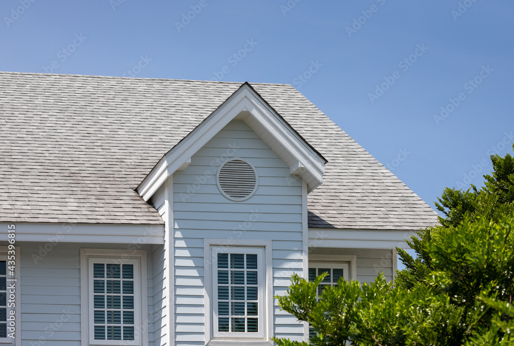 Roof shingles with garret house on top of the house among a lot of trees. dark asphalt tiles on the roof background