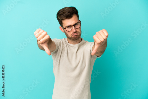 Young caucasian handsome man isolated on blue background showing thumb down with two hands