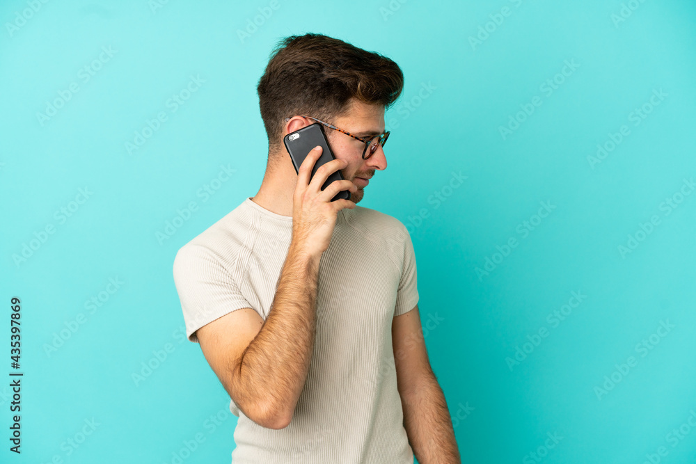 Young caucasian handsome man isolated on blue background keeping a conversation with the mobile phone with someone Young caucasian handsome man isolated on blue background keeping a conversation with the mobile phone with someone
