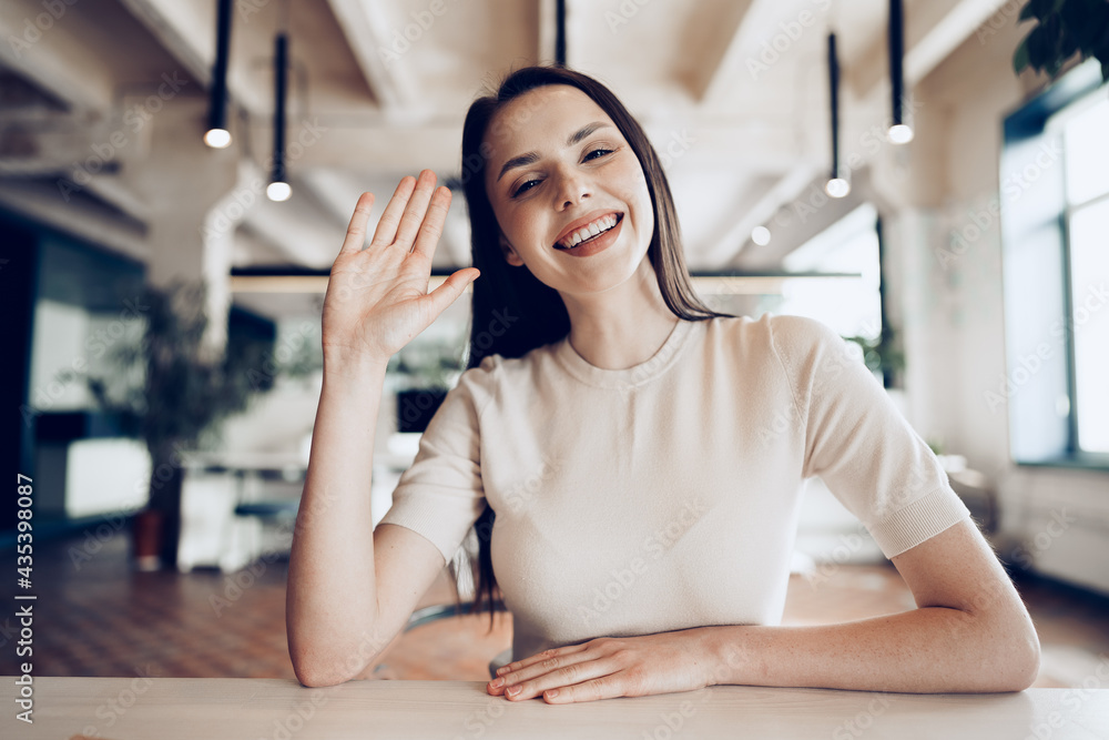 Portrait of attractive smiling businesswoman waving hand, looking at camera