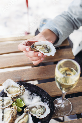 Holding an oyster, a plate of oysters, a glass of sparkling wine on a wooden table 