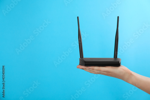 Foto Woman holding modern Wi-Fi router on light blue background, closeup