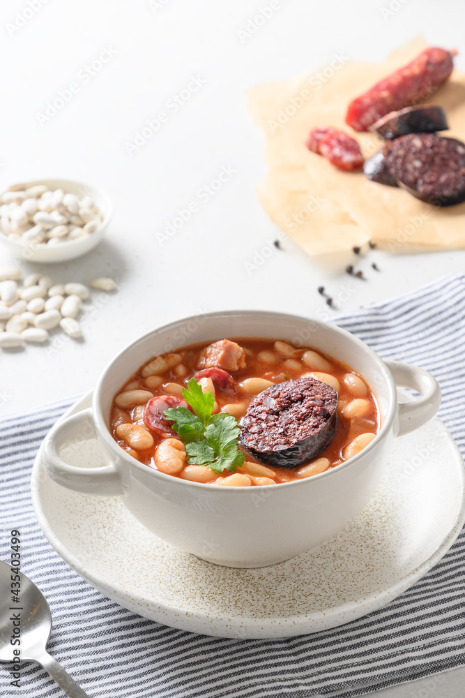 Asturiana traditional fabada with haricot, blood sausage on a white table. Vertical orientation. Spanish cuisine. Close up. Asturiana traditional fabada with haricot, blood sausage on a white table. Vertical orientation. Spanish cuisine. Close up.