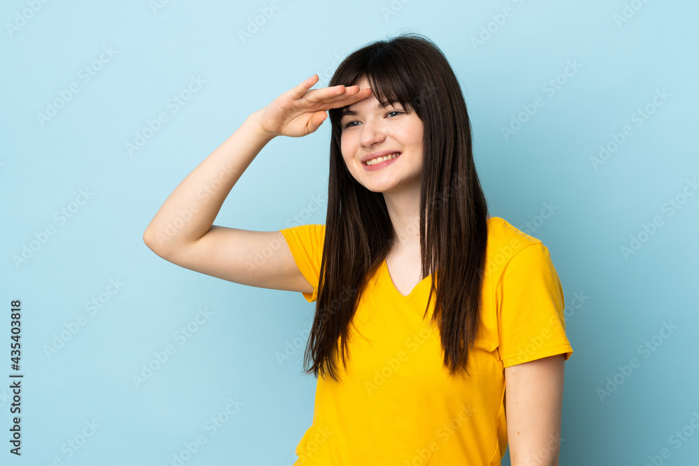 Teenager Ukrainian girl isolated on blue background saluting with hand with happy expression Teenager Ukrainian girl isolated on blue background saluting with hand with happy expression