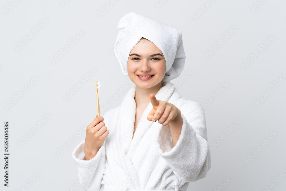 Young woman in a bathrobe holding toothbrush points finger at you with a confident expression Young woman in a bathrobe holding toothbrush points finger at you with a confident expression