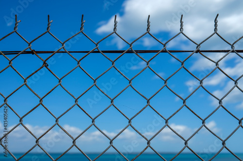 Sea and blue sky behind a chain link chainwire fence