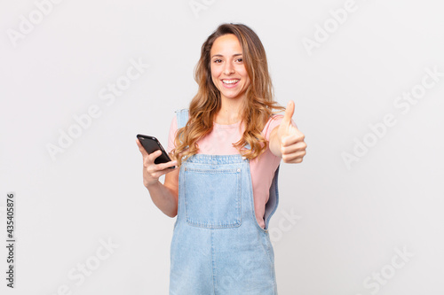 pretty woman feeling proud,smiling positively with thumbs up and holding a smartphone photo