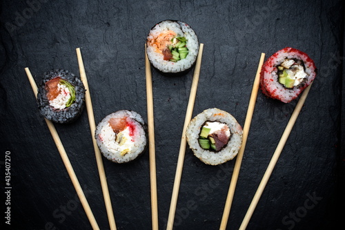 different sushi rolls on a black background with chopsticks