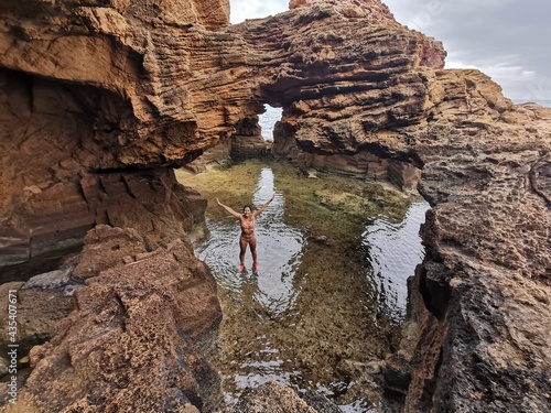 Woman in bikini raises her arms happily enjoying the adventure of finding caves at the edge of the sea photo