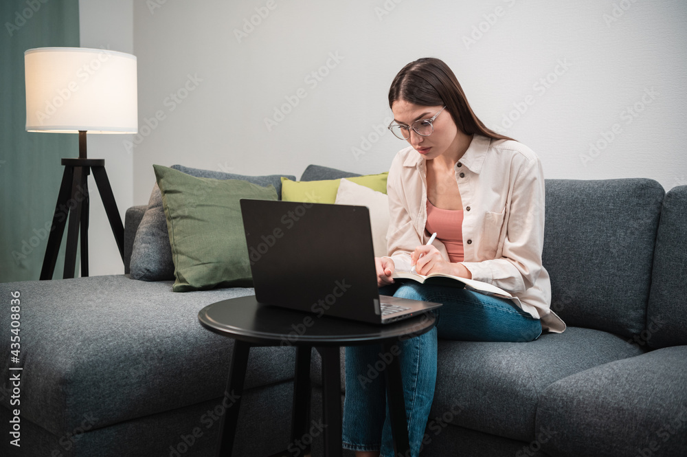 A pretty woman conducts a webinar from home, she sits on the couch and communicates using a laptop A pretty woman conducts a webinar from home, she sits on the couch and communicates using a laptop