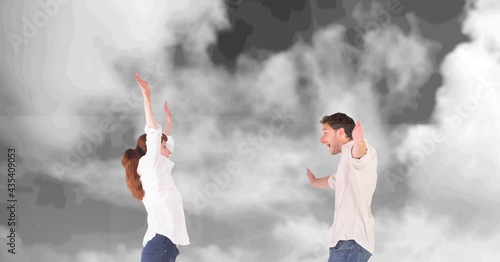 Composition of happy couple celebrating with arms outstretched over black and white cloudy sky