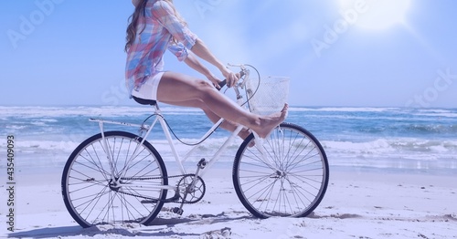 Composition of woman riding bike on beach with copy space