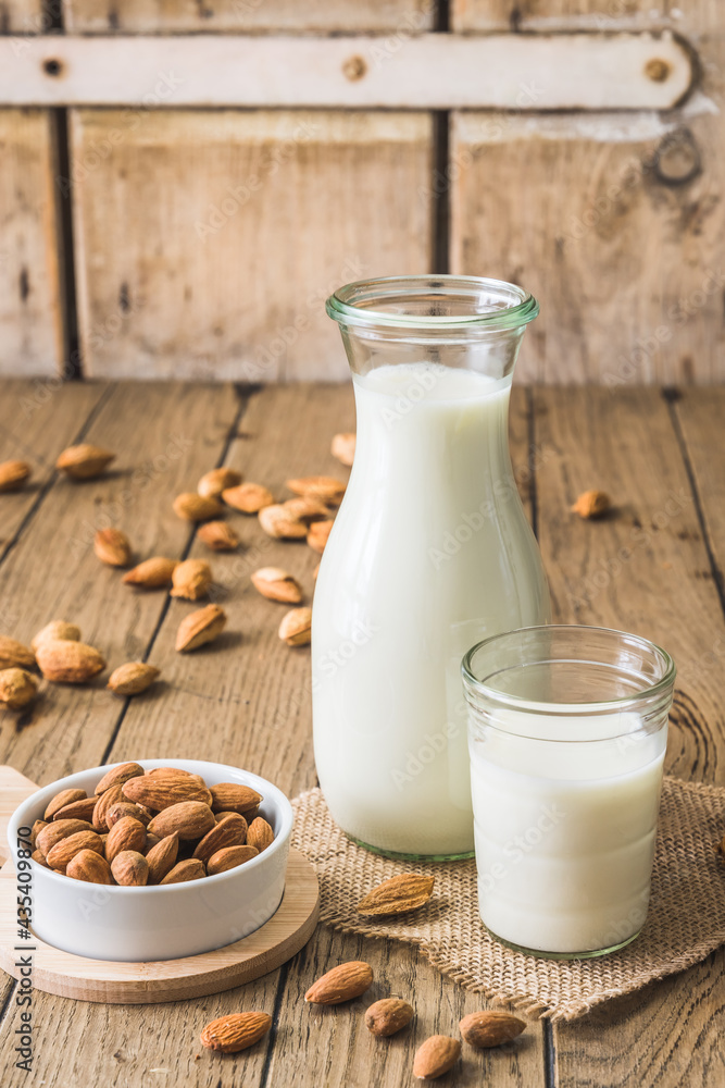 Glass and pitcher with vegan almond milk, almond kernels and whole almonds on an old rustic wooden table, vertical Glass and pitcher with vegan almond milk, almond kernels and whole almonds on an old rustic wooden table, vertical