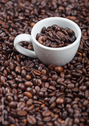 White espresso cup with fresh raw coffee beans inside beans background.