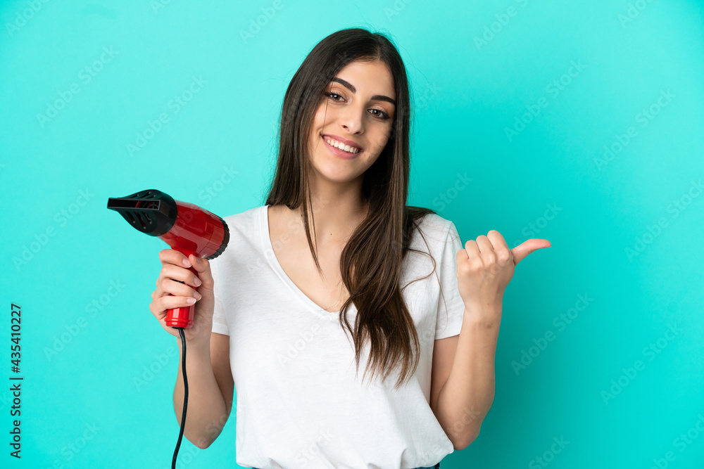 Young caucasian woman holding a hairdryer isolated on blue background pointing to the side to present a product Young caucasian woman holding a hairdryer isolated on blue background pointing to the side to present a product
