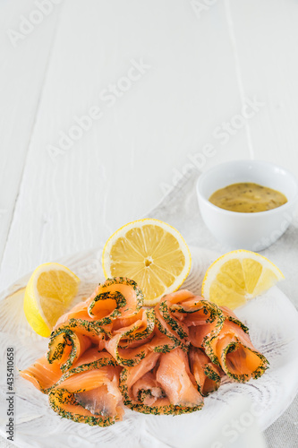Smoked salmon rolls with lemon on white plate and mustard dip in white bowl on white wooden background, vertcial stock photo with copy space