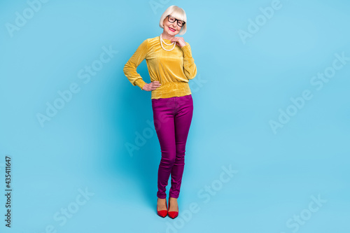 Full size photo of nice short hairdo elder lady stand wear blouse eyewear pants isolated on blue color background