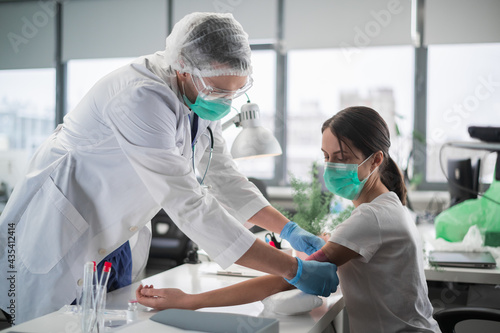 A medical student takes blood from a vein for analysis from a young woman in a laboratory