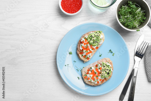 Delicious sandwiches with caviar, cheese, avocado and microgreens on white wooden table, flat lay. Space for text © New Africa