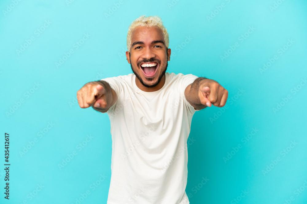 Young Colombian handsome man isolated on blue background surprised and pointing front Young Colombian handsome man isolated on blue background surprised and pointing front