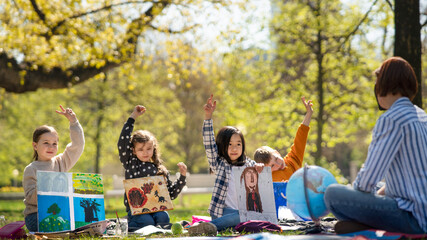Small children with teacher outdoors in city park, learning group education and art concept.