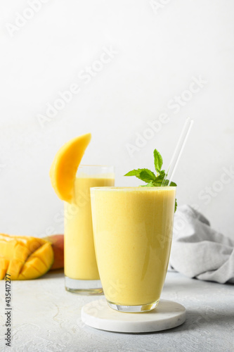 Two mango lassi in glasses on gray background. Indian healthy vegan beverage with mango. Freshness lassi made of yogurt, water, spices, fruits and ice.
