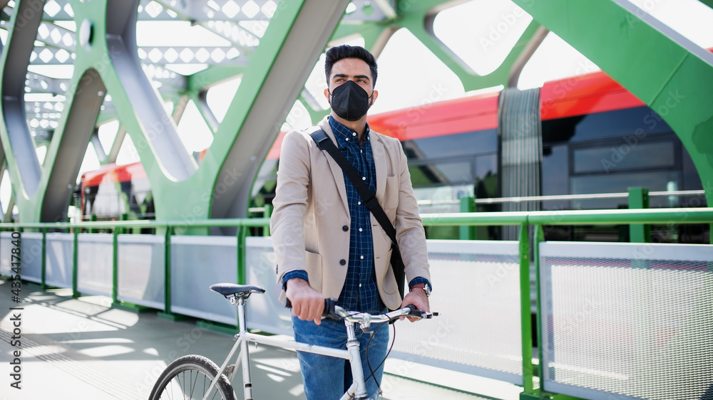 Young business man commuter with bicycle going to work outdoors on bridge in city, coronavirus concept.