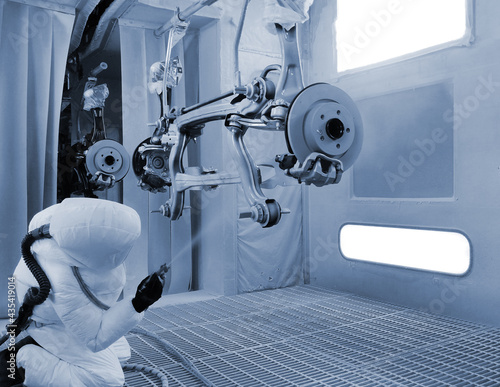 An Asian mechanic is using a car suspension spray gun to prevent rust in the paint room. Specially controlled