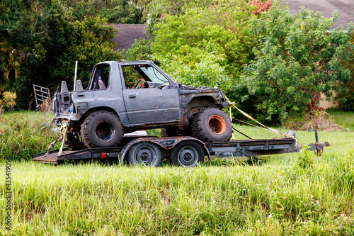 Canvas-taulu Four wheel drive jeep type truck with oversized jumbo dirt tires on a motor boat trailer rusted, missing fenders and exterior panels, rusted and with no tailgate on blocks in grass, and weed yard
